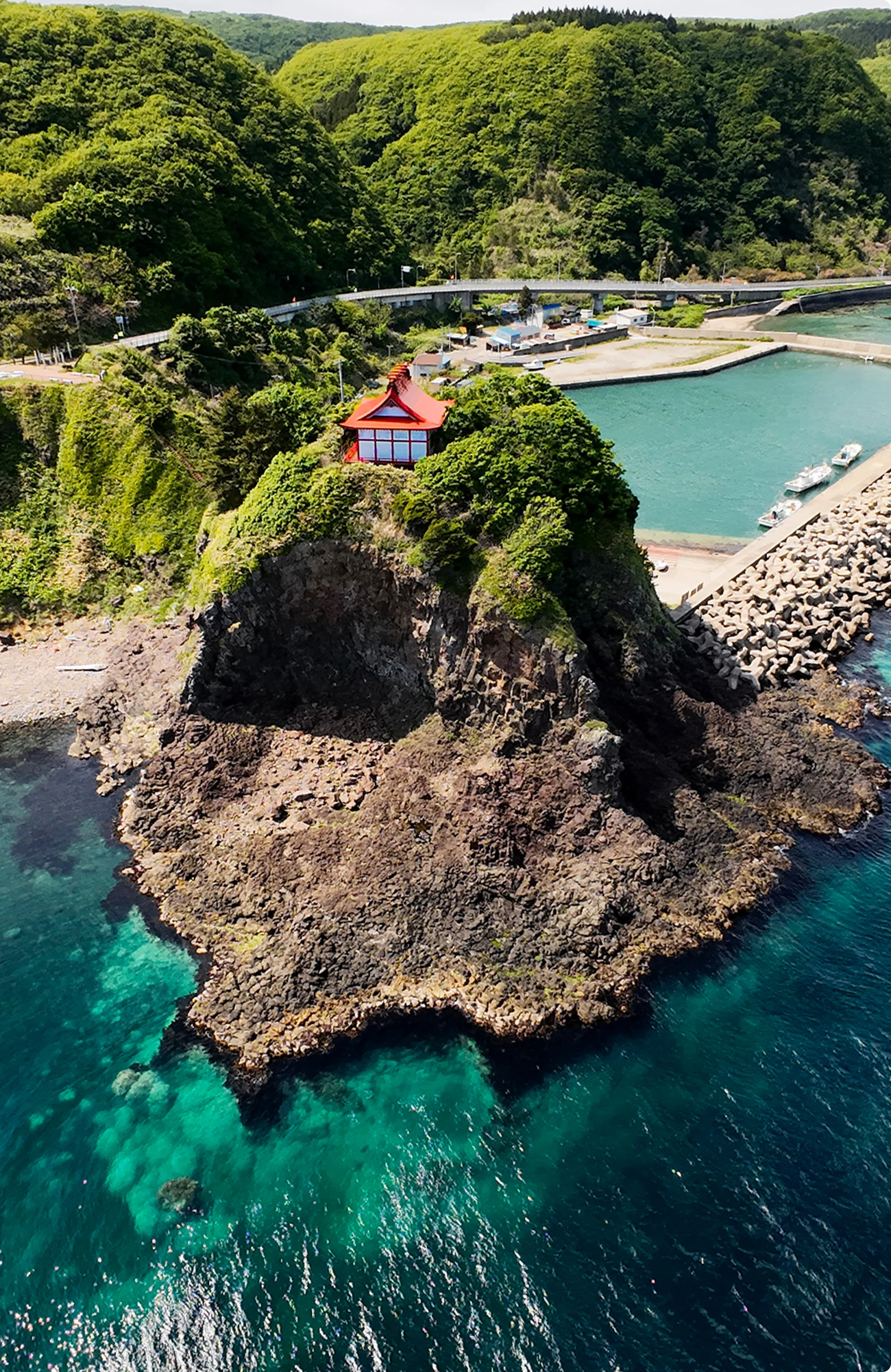 海に突き出た岩場の上に建つ赤い屋根の神社と青い海